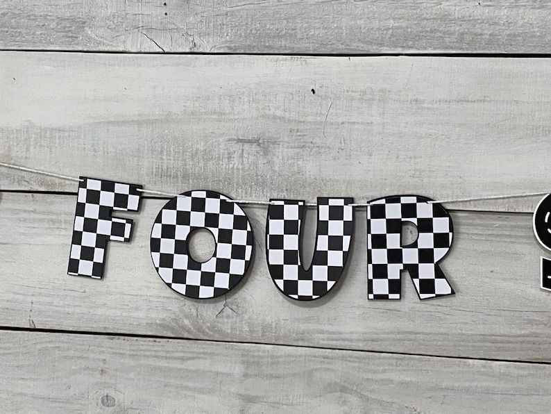 Op de afbeelding: Zwart-wit geblokt spandoek met het woord "VIER" in grote letters. Het spandoek is aan een wit touw bevestigd en hangt tegen een witte houten achtergrond.