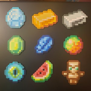 May include: Nine colorful pixel art designs, including a blue diamond, a gold bar, a silver bar, a green emerald, a blue lapis lazuli, a red and orange pumpkin, a blue eye, a watermelon slice, and a brown wooden totem.
