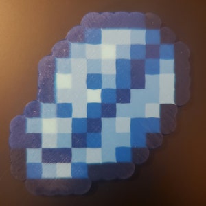 May include: A blue and white pixelated design made of small plastic beads. The design is shaped like a cloud.
