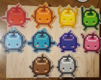 May include: Ten colorful pixel art characters, each with a different color and design, are displayed on a wooden surface. The characters are all in the shape of a small, round creature with a big head and small body. The colors of the characters are red, orange, yellow, green, blue, purple, pink, brown, and gray.