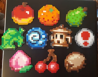 May include: A collection of 11 colorful pixel art designs, including a red apple, an orange, a green pear, a green leaf, a blue swirl, a brown building, a red and white mushroom, a pink peach, a red cherry, a brown mushroom, and a brown rock.