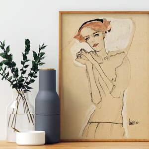 May include: A framed black and white line drawing of a woman with red hair wearing a white collar. The woman is looking down with her hands clasped in front of her. The drawing is on a beige background and signed "Klimt 10."