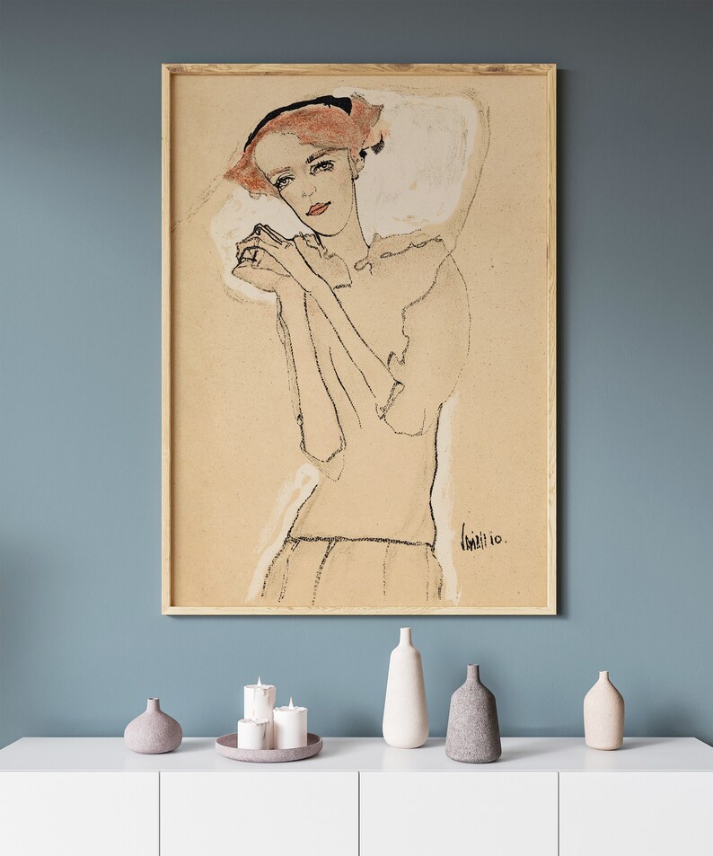 May include: A framed black and white line drawing of a woman with red hair wearing a white dress. The drawing is on a beige background and the artist's signature is visible in the bottom right corner.