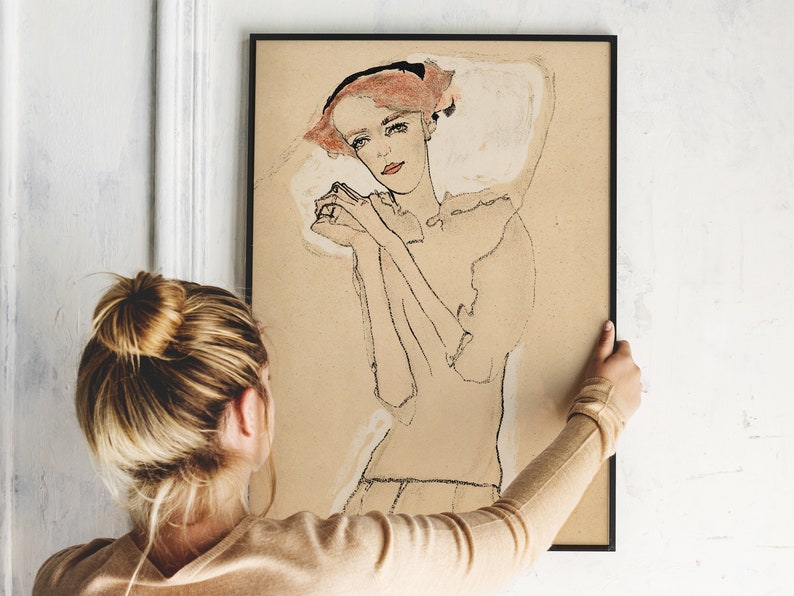 May include: A black framed print of a line drawing of a woman with red hair, wearing a white blouse, with her hands clasped in front of her.