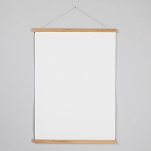 May include: A white poster hanging on a light gray wall in a wooden frame with a string attached to the top.