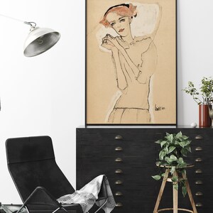May include: A black and white line drawing of a woman with red hair wearing a white dress. The drawing is framed in a black frame and hanging on a white wall.