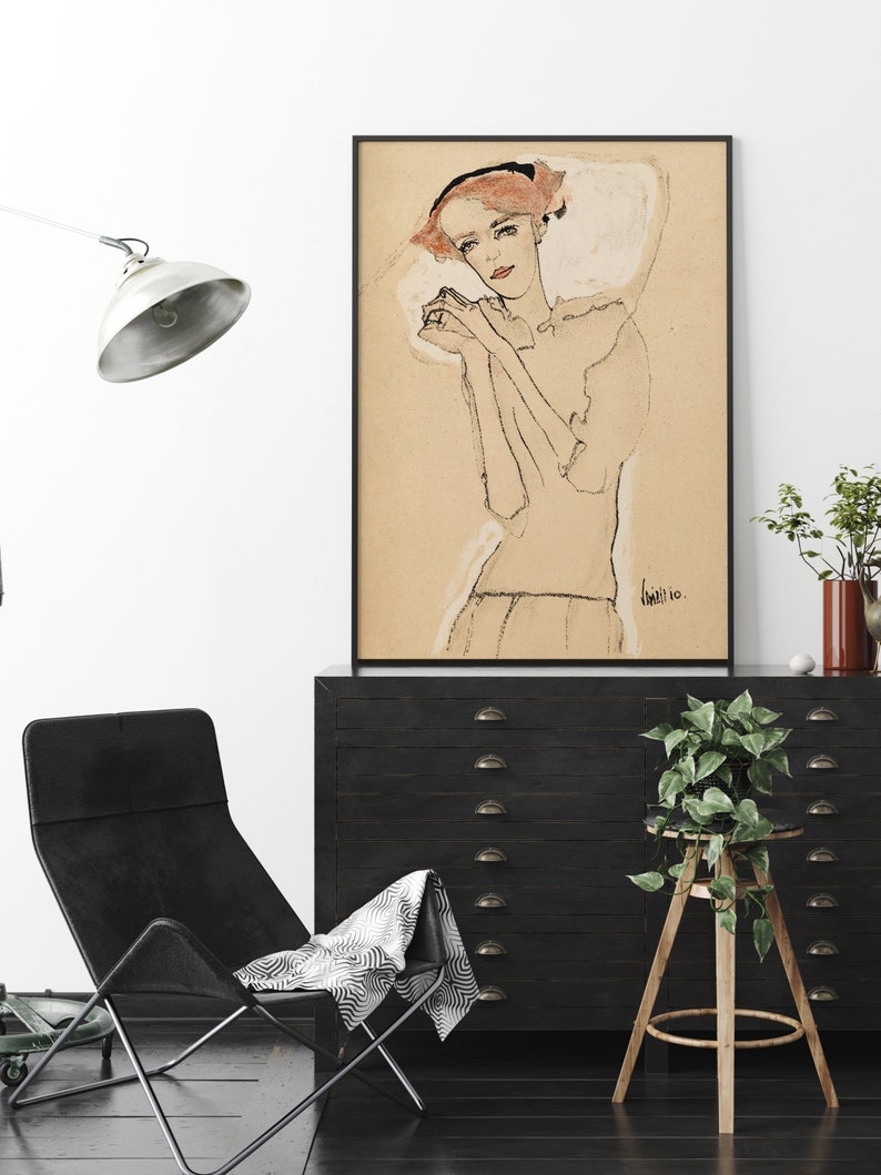 May include: A black and white line drawing of a woman with red hair wearing a white dress. The drawing is framed in a black frame and hanging on a white wall.