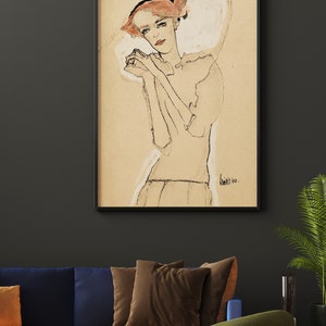 May include: A black and white drawing of a woman with red hair, wearing a white dress and a black headband. The drawing is framed in a black frame and is hanging on a dark gray wall.