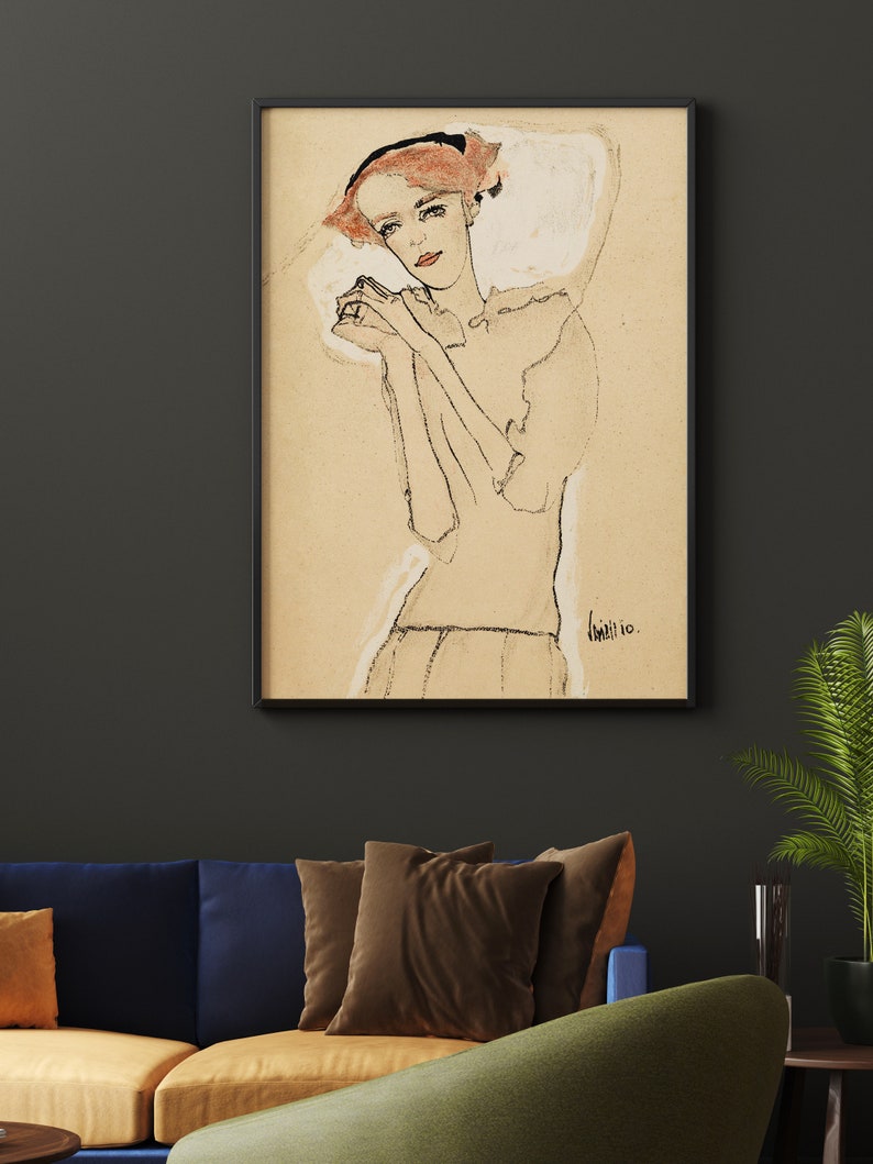 May include: A black and white drawing of a woman with red hair, wearing a white dress and a black headband. The drawing is framed in a black frame and is hanging on a dark gray wall.