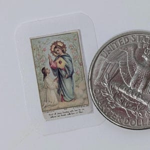 May include: A small, vintage religious card featuring a depiction of a saintly figure in blue robes with a halo, interacting with a kneeling person. The card is in a clear plastic sleeve, next to a US quarter for size comparison. The image has a floral background.