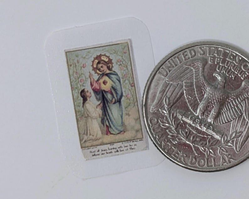 May include: A small, vintage religious card featuring a depiction of a saintly figure in blue robes with a halo, interacting with a kneeling person. The card is in a clear plastic sleeve, next to a US quarter for size comparison. The image has a floral background.