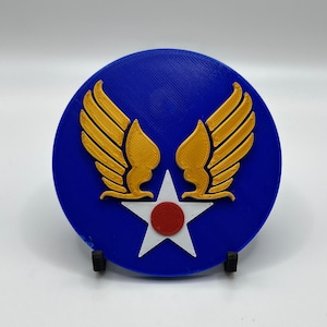 May include: A blue circular coaster with a white star and red center, surrounded by two gold wings. The coaster is on a black stand.