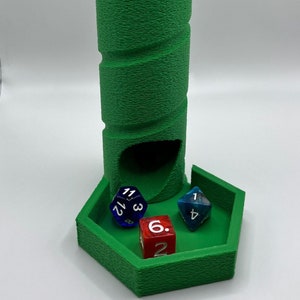 May include: A green, textured dice tower with a hexagonal base and a cylindrical tower. A red twenty-sided die sits atop the tower, with three multi-sided dice in the tray below. The dice are blue, red, and blue-green.