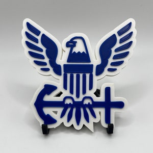 May include: A blue and white 3D printed eagle with an anchor and cross, representing the United States Coast Guard.