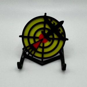 May include: A black and yellow target with a red bullseye and a black silhouette of a plane flying through the center. The target is mounted on a black stand.