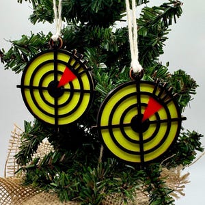 May include: Two radar-themed Christmas decorations. Each decoration features a yellow circular background with black concentric circles and a red triangle. They hang from a Christmas tree with twine.