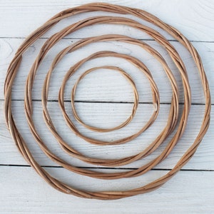 Puede incluir: Cuatro aros de mimbre trenzado marrón de diferentes tamaños, anidados uno dentro del otro, sobre un fondo de madera blanca.