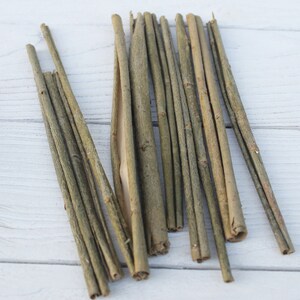 May include: A bundle of thin, light brown twigs, arranged in a fan shape on a white wooden surface.