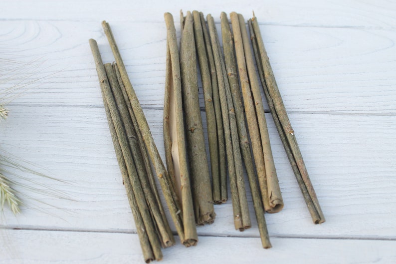 May include: A bundle of thin, light brown twigs, arranged in a fan shape on a white wooden surface.