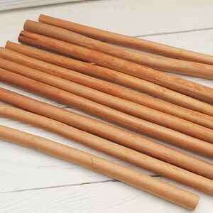 Peut inclure: Un groupe de 12 b&acirc;tonnets de cannelle naturelle, dispos&eacute;s en &eacute;ventail sur une surface en bois blanc. Les b&acirc;tonnets sont bruns et ont une texture rugueuse.