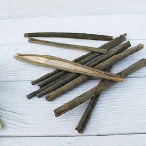 May include: A pile of thin, brown, wooden sticks on a white wooden surface. Some of the sticks are split open, revealing a lighter interior.