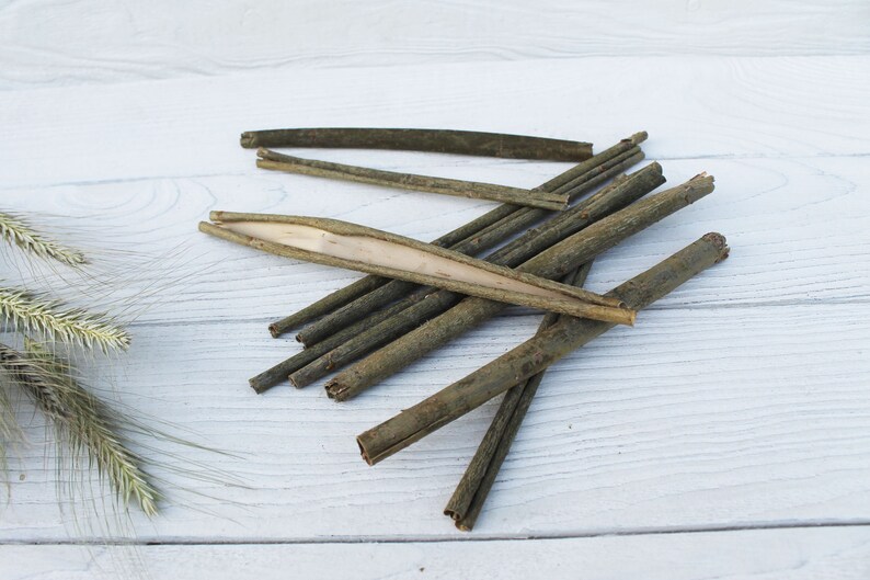 May include: A pile of thin, brown, wooden sticks on a white wooden surface. Some of the sticks are split open, revealing a lighter interior.