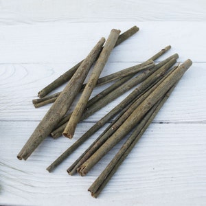 May include: A bundle of thin, brown twigs on a white wooden surface. The twigs are arranged in a fan shape, with the tips pointing towards the right side of the image.