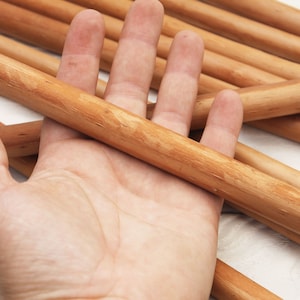 Peut inclure: Une main tenant un paquet de chevilles en bois lisses de couleur brun clair. Les chevilles ont un diam&egrave;tre d'environ 1,2 cm et sont dispos&eacute;es en forme de croix.