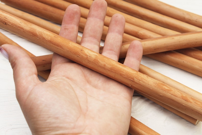 Peut inclure: Une main tenant un paquet de chevilles en bois lisses de couleur brun clair. Les chevilles ont un diam&egrave;tre d'environ 1,2 cm et sont dispos&eacute;es en forme de croix.