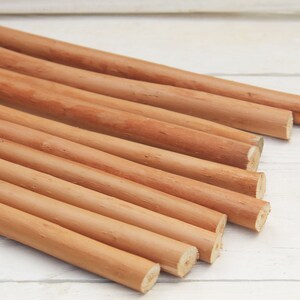 Peut inclure: Un groupe de 10 chevilles en bois lisses de couleur brun clair, dispos&eacute;es en &eacute;ventail sur une surface en bois blanc.
