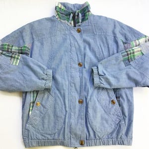 May include: Light blue denim jacket with a stand-up collar and button closure. Features plaid fabric accents on the collar and sleeves. Includes two front pockets and elastic cuffs. A casual, vintage-style outerwear piece.