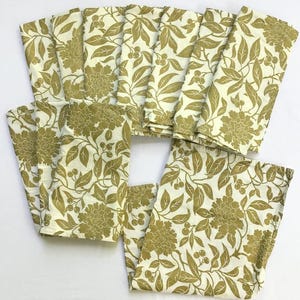 May include: A collection of cream-colored cloth napkins with a repeating floral pattern in shades of gold. The design features large flowers, leaves, and berries. The napkins are neatly folded and arranged, showcasing the intricate botanical print.