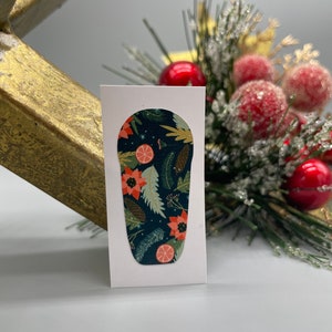 Könnte beinhalten: Ein dunkelblauer Nagelaufkleber mit einem festlichen Weihnachtsdesign mit roten Weihnachtssternen, grünen Blättern und orangen Zitrusscheiben. Das Design ist auf einem dunkelblauen Hintergrund mit weißen Schneeflocken.