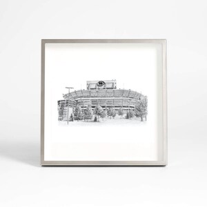 May include: A black and white framed print of a football stadium. The stadium is drawn in a realistic style and features a large scoreboard with a logo.