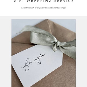 Puede incluir: Una bolsa de regalo de papel marr&oacute;n con una cinta verde salvia atada en un lazo. Una etiqueta de regalo blanca est&aacute; unida a la cinta con las palabras "para ti" escritas en caligraf&iacute;a negra.
