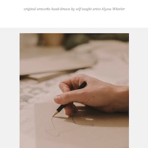 May include: A hand draws a line on a piece of paper with a black pencil. The paper is on a table with other papers visible in the background. The image is in a warm, natural light.