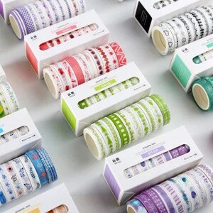 May include: Assortment of colourful washi tapes in various patterns, including floral, geometric, and stripes. The tapes are packaged in clear plastic rolls and come in sets of 6 or 12. The packaging features the text "Decorative Tape" and "Washi Tape".