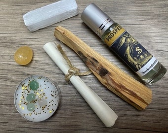 May include: A prosperity kit with a white selenite stick, a palo santo stick, a small white candle with green and pink crystals, a yellow citrine stone, a rolled up white paper with a twine bow, and a glass roller bottle with a black label that says "PROSPER" and "The Abundance Ritual".