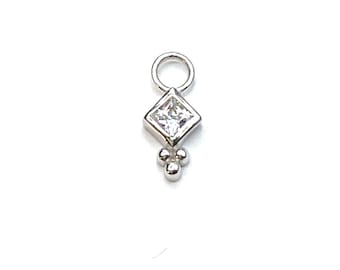 May include: A silver charm with a square, clear gemstone set in a diamond shape, with three small round accents below. The charm has a small loop at the top for attachment. Jewelry.