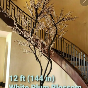 May include: A 12 ft (144 in) tall white plum blossom artificial tree in a white ceramic pot. The tree is displayed in a home setting with a staircase in the background.