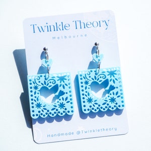 May include: A pair of light blue earrings with a cutout design featuring a bird and floral patterns. The earrings are handmade and have silver hooks.