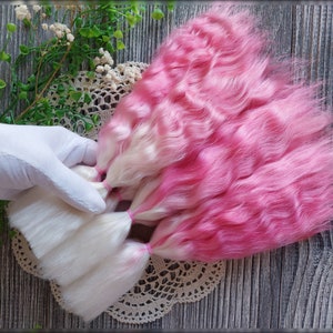 May include: A set of pink and white doll hair wefts. The wefts are wavy and have a gradient color from white to pink.