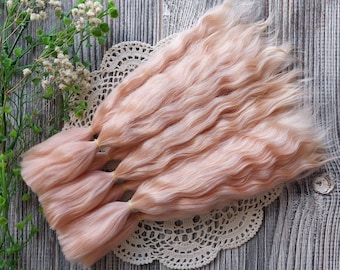 以下が含まれることがあります： 長い波状の薄いピンクのドールヘアの束が3つ。ゴムバンドで一緒に結ばれています。