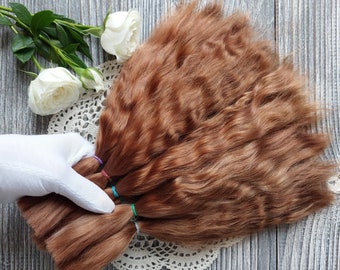 以下が含まれることがあります： カラフルなゴムで結ばれた、明るい茶色のヒューマンヘアーエクステンションの束。髪は扇形に配置され、白いレースのドイリーの上に置かれています。