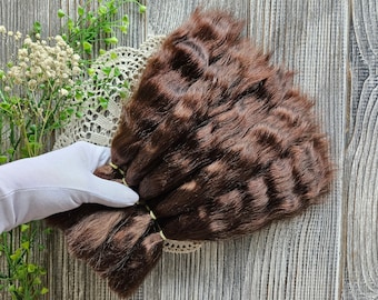以下が含まれることがあります： ゴムバンドでまとめられた茶色のヒューマンヘアーエクステンションの束。扇形に配置され、白いレースのドイリーの上に置かれています。