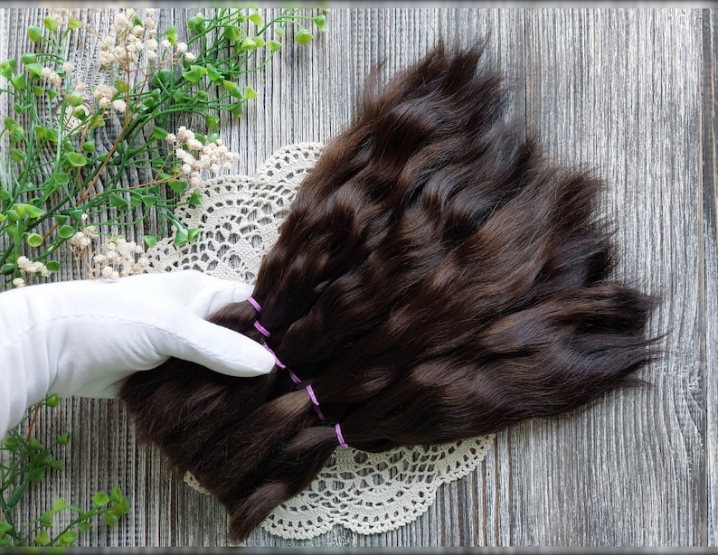May include: A bundle of dark brown human hair extensions tied with purple elastics. The hair is smooth and straight, and the ends are trimmed evenly.
