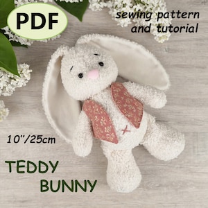 Puede incluir: Un patrón de costura en PDF y tutorial para un conejo de peluche de 25 cm. El juguete está hecho de tela texturizada color crema con orejas largas, ojos negros, nariz rosa, una pequeña cruz rosa bordada en la barriga y un chaleco floral.