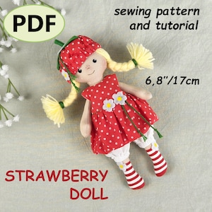 May include: A fabric doll measuring 17cm tall, featuring yellow yarn hair in braids, a red strawberry-patterned hat and dress with white polka dots, white bloomers, and red and white striped socks. Text reads PDF, sewing pattern and tutorial.