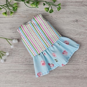 Completed doll outfit with colorful top and floral blue skirt displayed flat with decorative greenery