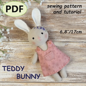 Peut inclure: Une poupée lapin en tissu beige portant une robe rose poudré à motifs floraux avec deux petits boutons sur les bretelles et une poche avant. Le lapin a des fleurs violettes brodées sur la tête et mesure 17 cm. Texte : PDF, sewing pattern and tutorial, TEDDY BUNNY.